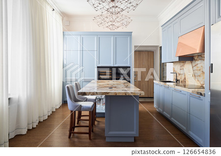 A modern kitchen featuring stunning blue cabinets complemented by a beautiful marble island 126654836