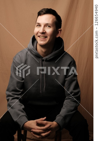 A Cheerful Young Man Wearing a Casual Hoodie is Sitting and Posing for a Portrait A Cheerful Young Man Wearing a Casual Hoodie is Sitting and Posing for a Portrait 126654940