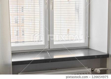 A modern window beautifully designed with stylish blinds and a sleek black Silestone window sill A modern window beautifully designed with stylish blinds and a sleek black Silestone window sill 126654975