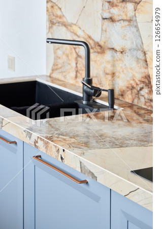 A modern kitchen sink has an elegant marble countertop and stylish faucet, enhancing its look A modern kitchen sink has an elegant marble countertop and stylish faucet, enhancing its look 126654979