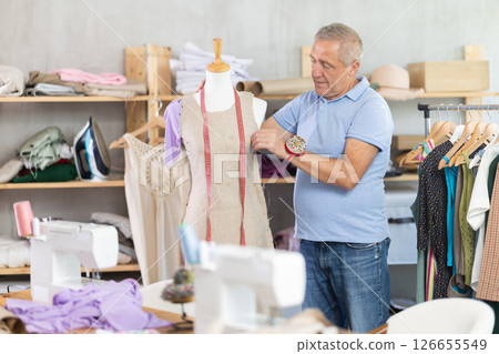 Male tailor standing in workshop checking dress Male tailor standing in workshop checking dress 126655549