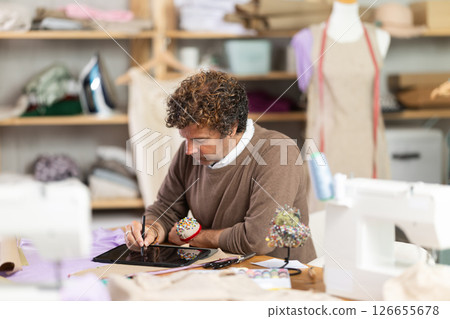 Man tailor creates sketch of dress on tablet Man tailor creates sketch of dress on tablet 126655678