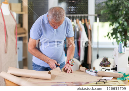 Elderly male tailor cutting out pattern from paper Elderly male tailor cutting out pattern from paper 126655709