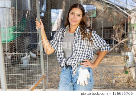 Young woman owner of livestock farm stands near corral mesh fence for livestock and rests 126655766