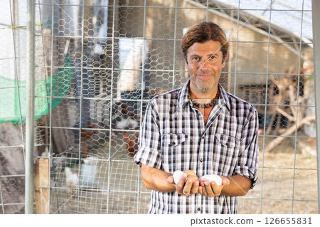 Positive male owner of farm company stands and holds in hands palms few fresh chicken eggs 126655831