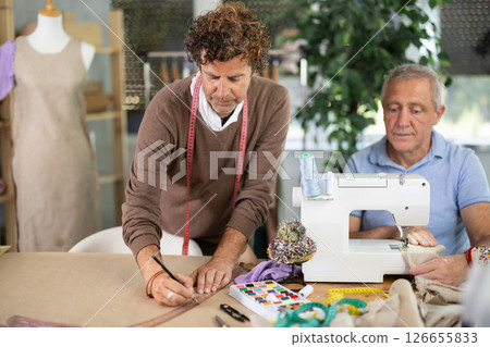Elderly man sews on machine male assistant drawing pattern 126655833