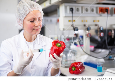 Middle-aged female scientist checking vegetables for harmful elements, injecting syringe into bell pepper in laboratory Middle-aged female scientist checking vegetables for harmful elements, injecting syringe into bell pepper in laboratory 126655933