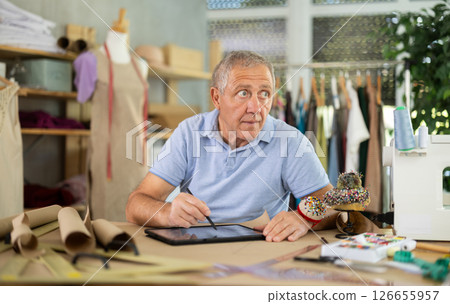 Mature man drawing on tablet in sewing salon 126655957