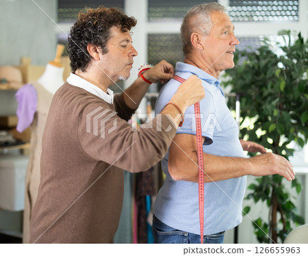 Adult man tailor takes body measurements from elderly man Adult man tailor takes body measurements from elderly man 126655963