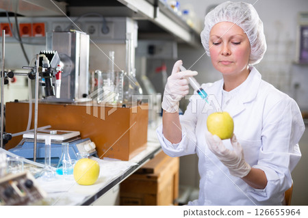 Adult female chemist makes an injection to a yellow apple Adult female chemist makes an injection to a yellow apple 126655964