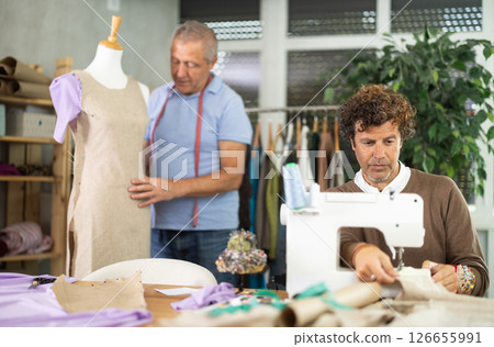 Adult man sews on machine male assistant sews on mannequin 126655991