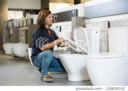 in plumbing department, male buyer checks for defects of toilet before purchasing toilet pan in plumbing department, male buyer checks for defects of toilet before purchasing toilet pan 126656102