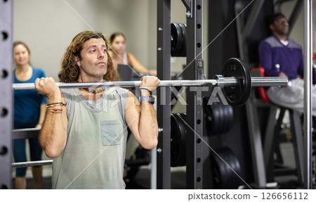 Caucasian sportsman doing squats with weight near squat rack in gym 126656112
