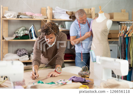 Adult man drawing pattern on paper male assistant sews on mannequin 126656118