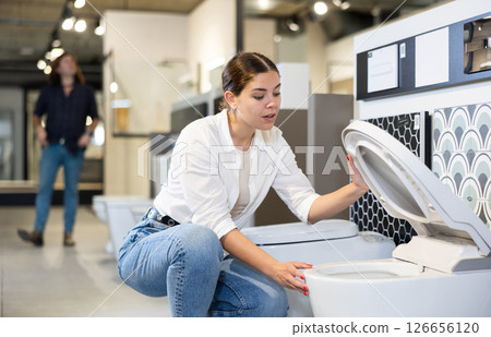 in plumbing department, female buyer checks for defects of toilet before purchasing toilet pan in plumbing department, female buyer checks for defects of toilet before purchasing toilet pan 126656120