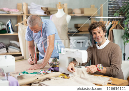 Adult man sews on machine male assistant drawing pattern 126656121