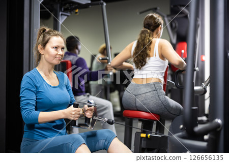 Woman is engaged in a simulator with horizontal weights in gym 126656135