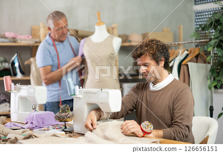 Adult man sews on machine male assistant sews on mannequin Adult man sews on machine male assistant sews on mannequin 126656151