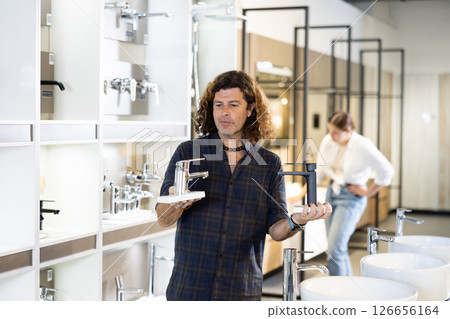 Man inspects and chooses new kitchen or bath tap faucet at hardware store Man inspects and chooses new kitchen or bath tap faucet at hardware store 126656164