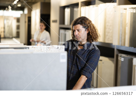 Handsome man in hardware store choosing floor ceramic tiles for his apartment Handsome man in hardware store choosing floor ceramic tiles for his apartment 126656317