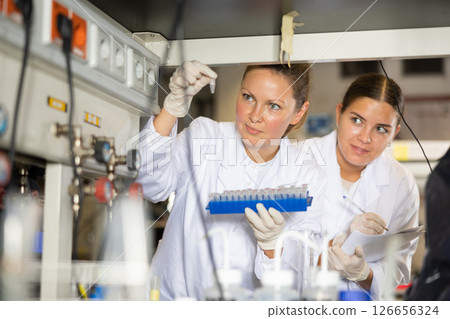 Adult and young female chemists examine liquid in beaker in laboratory 126656324