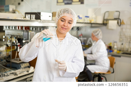 Female chemist working in laboratory, analyzing liquid samples in test flasks Female chemist working in laboratory, analyzing liquid samples in test flasks 126656351