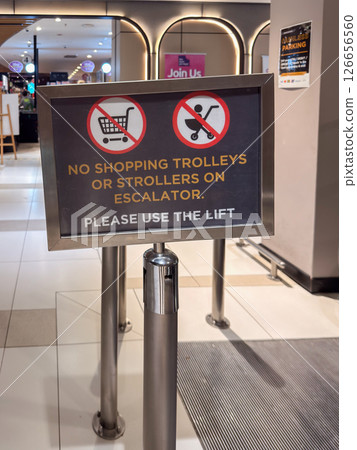Sign indicating no shopping trolleys or strollers allowed on escalators in a shopping center 126656560