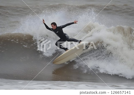 Extreme Surfing Action: Man Riding a Wave on a Surfboard in Wetsuit 126657141