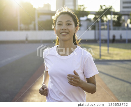 A scene of a woman running with a refreshing smile on her face on a sports field at dusk 126658732