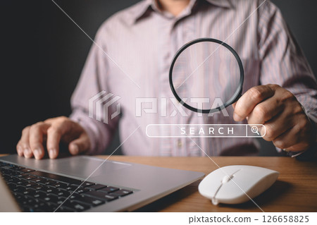 A person uses a magnifying glass near a laptop with a digital search bar overlay, symbolizing search engine optimization, focus, and the pursuit of information in a digital environment. A person uses a magnifying glass near a laptop with a digital search bar overlay, symbolizing search engine optimization, focus, and the pursuit of information in a digital environment. 126658825