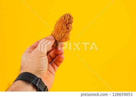 Lviv Ukraine 05.21.25 Hand holding crispy fried chicken against bright background Lviv Ukraine 05.21.25 Hand holding crispy fried chicken against bright background 126659051