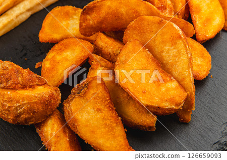 Crispy potato wedges served on a black plate Crispy potato wedges served on a black plate 126659093