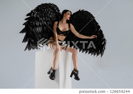 Woman in lingerie with dramatic black wings perched on a pedestal Woman in lingerie with dramatic black wings perched on a pedestal 126659244