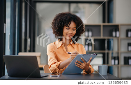 Confident business expert attractive smiling young woman typing laptop ang holding digital tablet  on desk in office. 126659685