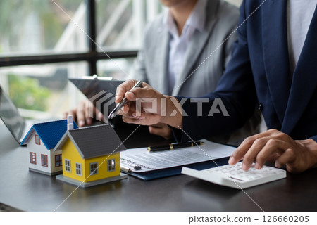 Buying a home or insurance deal, an insurance agent pointing a pen to those interested in renting a house, a contract, signing an Home buying agreement Buying a home or insurance deal, an insurance agent pointing a pen to those interested in renting a house, a contract, signing an Home buying agreement 126660205