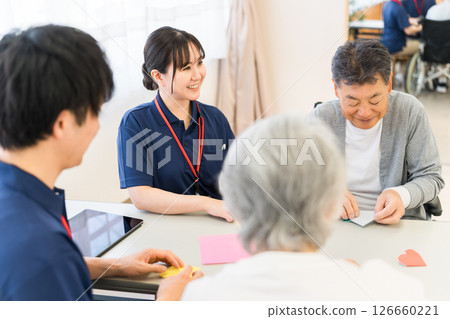 Senior men and women doing origami with male and female care staff working at a nursing home or care facility Senior men and women doing origami with male and female care staff working at a nursing home or care facility 126660221