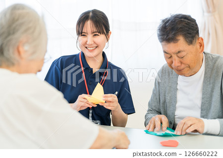老年男性和女性與養老院或護理機構的女性護理人員一起摺紙 126660222