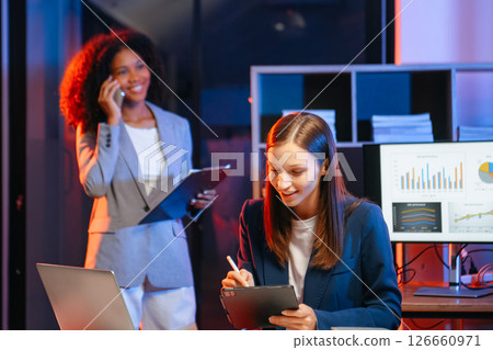 Two business workers talking on the smartphone and using laptop at the office. overtime 126660971
