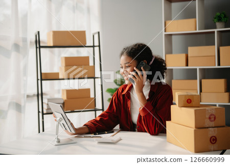 Young African woman running online store Startup small business SME, using smartphone or tablet taking receive and checking online purchase shopping order 126660999