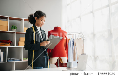 Diverse female fashion designers at work with tailor centimeters on necks and holds tablet and smartphone. independent creative design business. Diverse female fashion designers at work with tailor centimeters on necks and holds tablet and smartphone. independent creative design business. 126661089