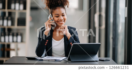 Beautiful Asian woman using laptop and tablet while sitting at her working place. Concentrated at work. 126661231