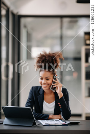 Beautiful Asian woman using laptop and tablet while sitting at her working place. Concentrated at work. Beautiful Asian woman using laptop and tablet while sitting at her working place. Concentrated at work. 126661232