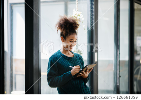 Confident female entrepreneur looking at the camera while standing. Young African woman standing in the boardroom of office. 126661359