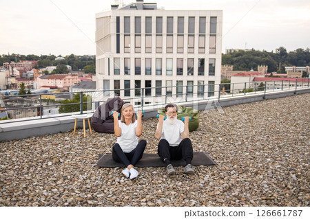 Senior man and woman sitting on rooftop platform exercising with dumbbells for fitness Senior man and woman sitting on rooftop platform exercising with dumbbells for fitness 126661787