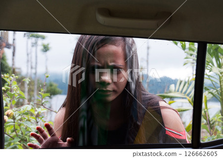 Scared woman looking through a car window in nature 126662605