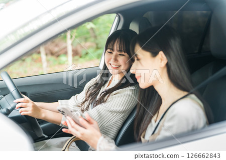 A woman driving a car and a woman in the passenger seat searching on a smartphone A woman driving a car and a woman in the passenger seat searching on a smartphone 126662843