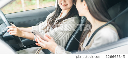 A woman driving a car and a woman in the passenger seat searching on a smartphone A woman driving a car and a woman in the passenger seat searching on a smartphone 126662845