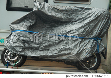 Motorcycle is covered with a grey plastic tarp 126662956