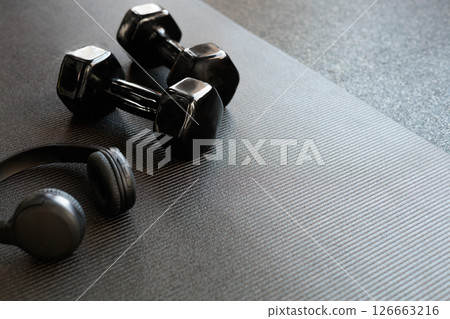 Headphones and black dumbbells lie on a black yoga mat. Flat lay. Space for text. 126663216