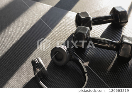 Concept of sports. Black headphones and dumbbells lie in the gym on a black yoga mat 126663219